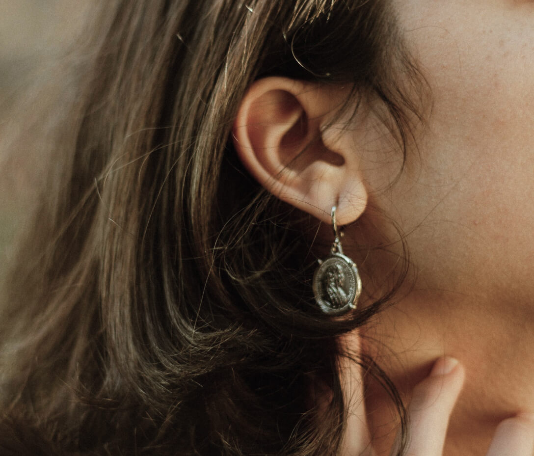 Antiqued coin drop earring worn on the ear