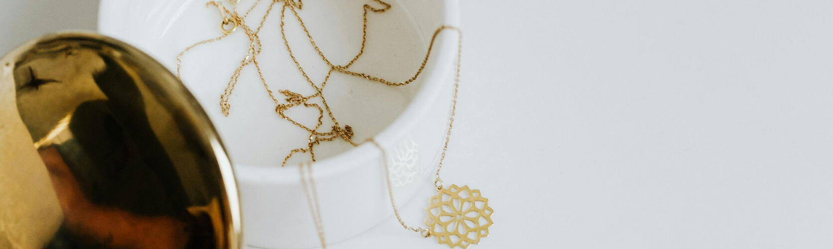 Fine gold chains and a filigree pendant in a ceramic dish