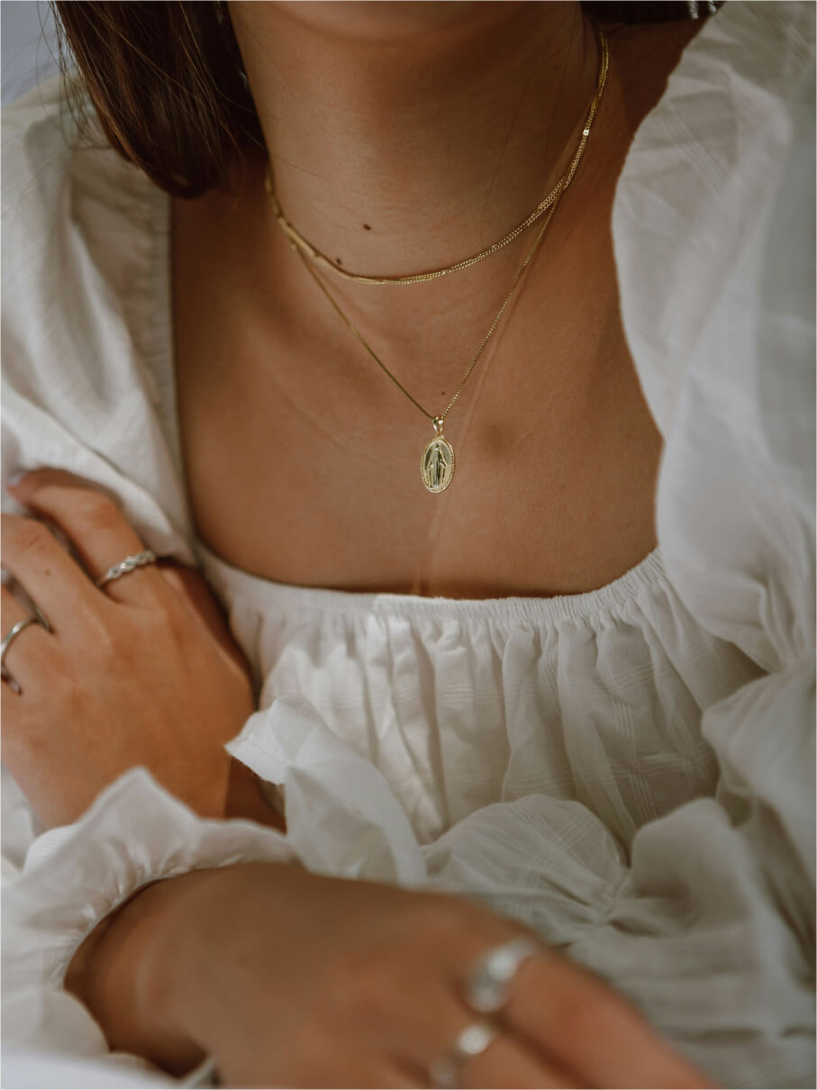 Gold oval medallion pendant layered over a herringbone chain